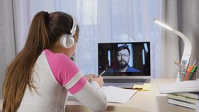 Girl with headphones learning online on computer, communicate with teacher, writing, distance education due quarantine time.
