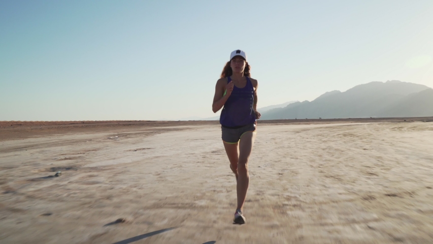 Young fit caucasian girl jogging in dry desert at sunrise