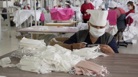 Women workers in a garment factory with medical masks on their faces sew protective masks during the COVID-19 virus pandemic. Fighting the COVID-19 pandemic. Shymkent / Kazakhstan - March 28 2020