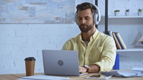 bearded man listening music in headphones near laptop in office
