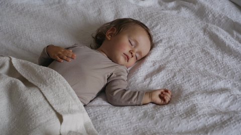 Peaceful  baby girl sleeping on  bed in a room. Soft focus. Sleeping baby concept. One year-old babygirl sleeps at home. Mom covers her daughter with a blanket