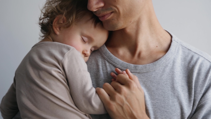 Father's Day. Close up portrait of a father and his daughter who sleeps in his arms. Father holds daughter's hand and smiles Royalty-Free Stock Footage #1049437009
