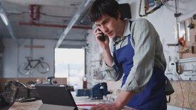 Male business owner in workshop using digital tablet and making call on mobile phone - shot in slow motion - Powered by Shutterstock - Get 15% off with code: PIKWIZARD15