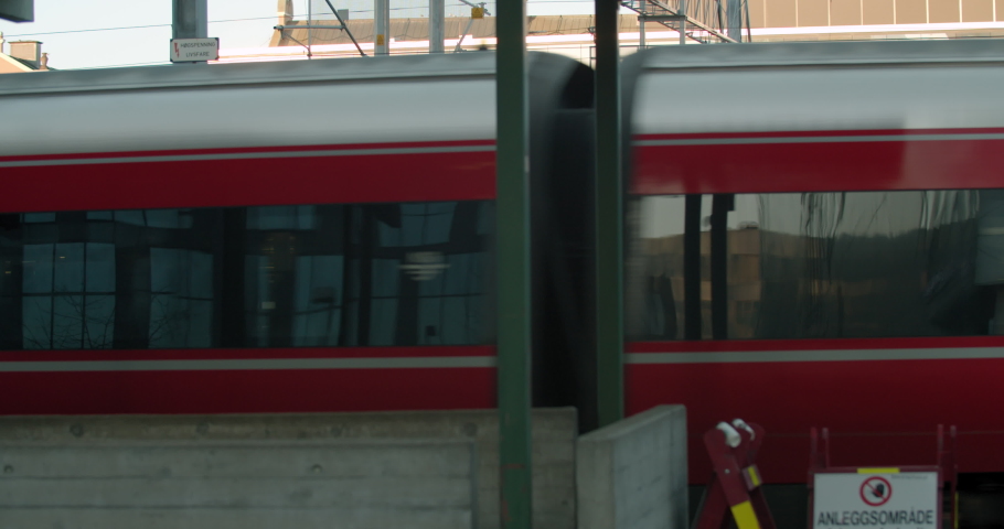 Close-up to wide shot with parallax motion of red train wagon set moving in front of empty terminal platform in yellow vibrant sunset at the central commerce train station in Bjørvika, Oslo Norway.