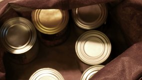 Food cans in fabric bag overhead soft focus, rubber gloved hand sharp focus cleans can with yellow cloth & puts it in bag with other cans, hand reaches across holding US bills gloved hand takes them - Powered by Shutterstock - Get 15% off with code: PIKWIZARD15