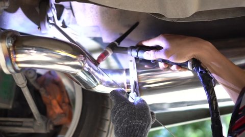 Asian welder welds car exhaust pipe