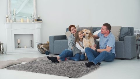 Parents with Daughter and Labrador Retriever Dog Relaxing near Sofa. Father Playing with Dog in the Living Room. Slow Motion. Pets and Animals Concept