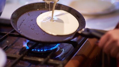 housewife prepares pancakes in a frying pan and a gas stove