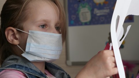 Quarantine, the threat of coronavirus. A child in a medical mask sits at a table and cuts out of paper. Quarantine homework.
