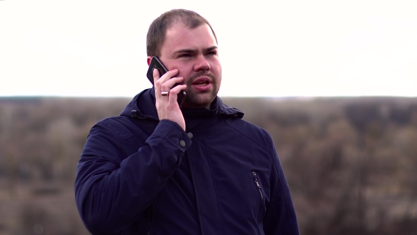 A man stands in a field and talking on the phone. Nature