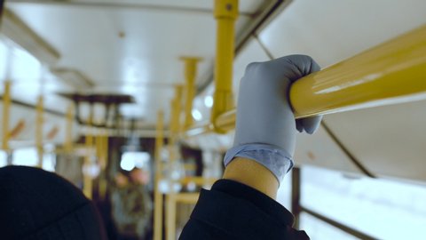 A man rides in a public transport bus and holding on to a handrail in his protective medical glove. Coronavirus covid-19 infection and epidemic protection concept. Pandemic. Closeup shot