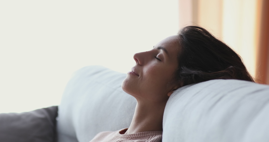 Healthy serene young woman leaning on cozy sofa taking deep breath of fresh clean air. Calm lady relaxing on comfortable couch, napping, enjoying no stress concept at home, close up side face view. Royalty-Free Stock Footage #1049471794