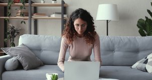 Excited young woman winner looks at laptop celebrates online success sits on sofa at home. Euphoric lady gets new distance job opportunity, reads good news in email, rejoices victory, feels motivated.
