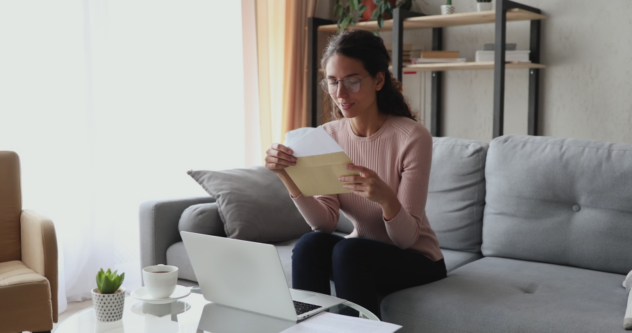Happy excited woman reads good news in mail letter sits on sofa at home. Overjoyed lady winner holds bank paper receiving approved loan, tax refund or salary notice, celebrating success concept. Royalty-Free Stock Footage #1049471815