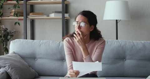 Stressed worried young woman reading bad news in paper mail letter at home. Desperate lady frustrated about bankruptcy, financial problem, receiving bank debt penalty, high bills, lost job concept.