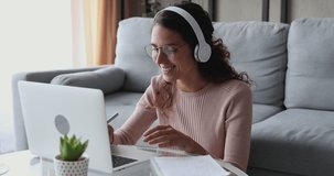 Young woman wearing headphones distance learning course, doing remote telework concept working from home office. Female student, online teacher conference calling by web cam using laptop making notes.