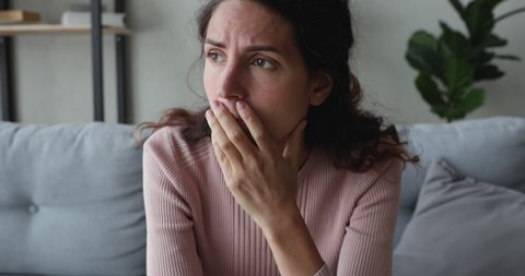 Depressed young woman feels stress concerned about psychological problem sitting alone on sofa at home. Frustrated worried millennial girl suffers from anxiety, despair or shame concept. Close up view