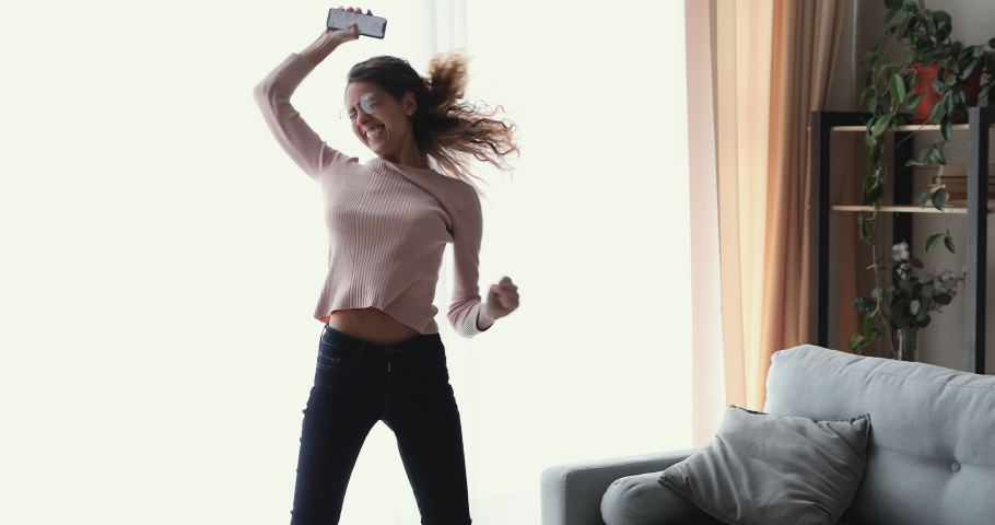 Funny overjoyed young woman winner jumping, dancing at home celebrating mobile win concept. Euphoric girl student receiving sms message reading great news. Happy female customer excited about success.