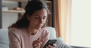 Smiling millennial woman watching funny video stories on smart phone at home. Happy female customer doing mobile shopping, reading news, using apps, surfing internet looking at cell sitting on couch.