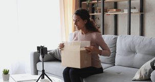 Young woman vlogger recording beauty unboxing vlog on smartphone. Female social media influencer unpacking delivery box with makeup accessories shooting cosmetic review video blog at home concept.