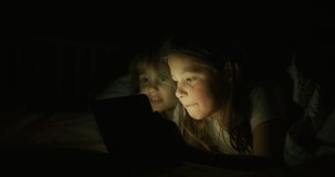 Close up shot of two little girls are using a tablet or smartphone in the dark. Concept. future of web technology, video technology, connections and vision of the future of children with web, gaming