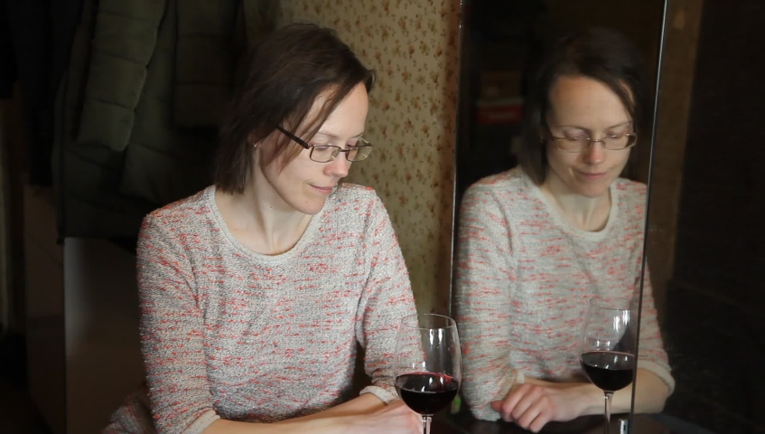 Woman is drinking wine with her reflection in mirror. Lonelines. 