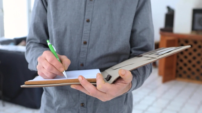 slow motion close up shot of man's hands holding a pen and clipboard as he taking notes with an interior background. inspector during home inspection. Royalty-Free Stock Footage #1049488588