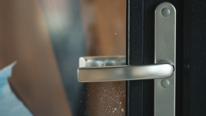 A hand in a protective glove on the handle of the front door. Protections in the midst of an epidemic