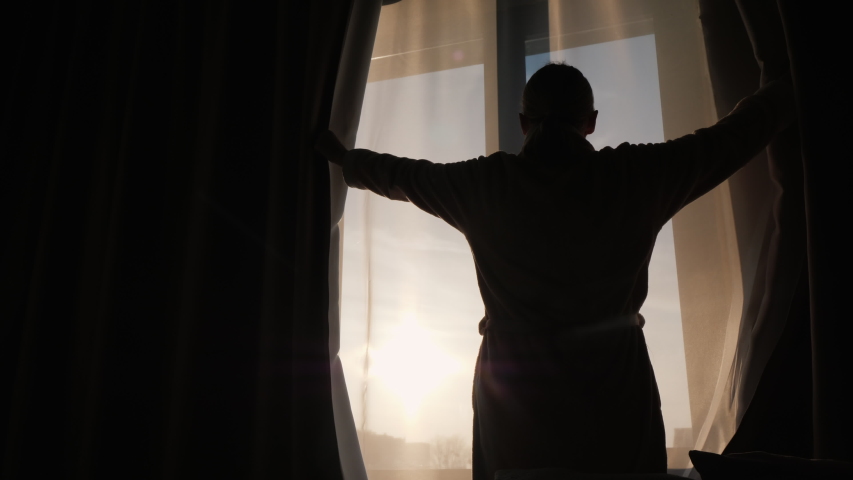 Woman opens curtains on window, meets new day