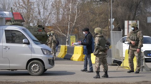 Almaty, Kazakhstan - March 20, 2020: Medical masked soldiers let cars through at a checkpoint in a coronavirus quarantined city. Armored personnel carrier and a police car stand in the background.