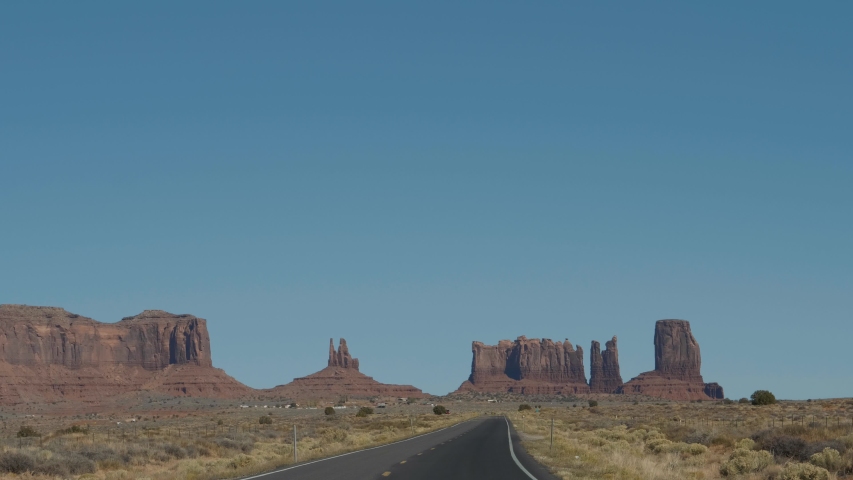 Pov from driving car on famous western black asphalt road with yellow marking going to monument valley of cliffs and rock formations of Mesa buttes in wild west of Usa in dry desert. Slow motion