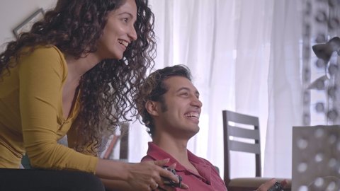 A young happy attractive married couple holding joysticks in their hands and playing an online video game together in the house. A smiling laughing man and woman spending time with each other indoors