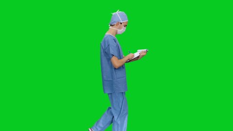 Side view of doctor in mack and uniform writing on clipboard while walking against green screen background, Chroma key 
