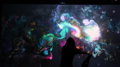 Girl plays with interactive video installation, New art form, generative graphics. Silhouette of girl draws multi-colored paints interactive installation. Woman does concept art with augmented reality