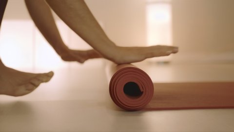 Closeup woman hands rolling up yoga mat after training in studio. Unrecognizable barefoot girl folding fitness mat on floor at yoga studio in slow motion