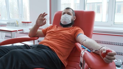 Blood donor makes okay gesture. Mature man with beard showing ok sign and looking at the camera. Male gripping squeezing red heart stress ball. Blood donation concept 4k
