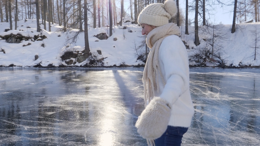 Young woman ice skating on frozen lake in winter. Female on ice skates surrounded by stunning mountain landscape. Natural frozen lake in the Alps. Woman enjoying winter season 