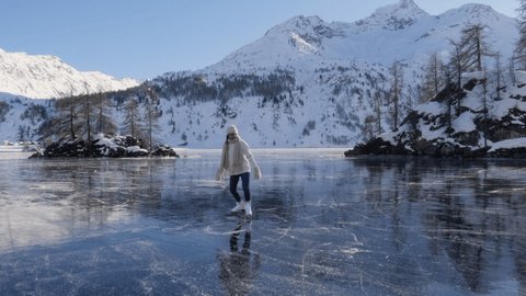 Young woman ice skating on frozen lake in winter. Female on ice skates surrounded by stunning mountain landscape. Natural frozen lake in the Alps. Woman enjoying winter season  Stock Video