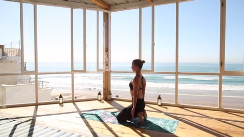 Skinny beautiful fit yoga woman in leggings and sport bra is practicing on yoga mat yoga poses in yoga studio with a view on the ocean, sunny day - fitness, sport and healthy lifestyle concept