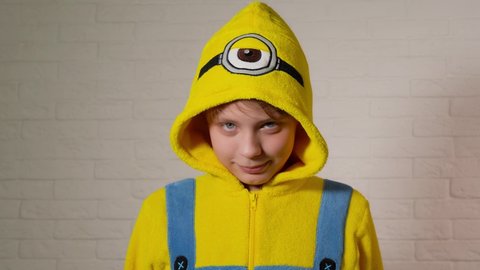 Chernihiv, Ukraine - January 16, 2020: Closeup view 4k video portrait of cute happy funny kid dressed in blue and yellow minion costume looking at camera happily and pointing at one eye on his head.