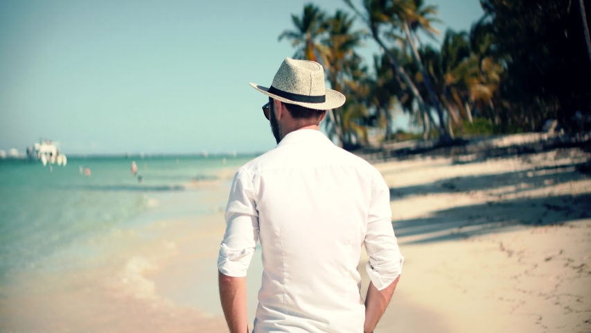 Beautiful Tanned Man In Hat Healthy Skin Sunbathing Enjoy Ocean Vacation. Happy Businessman Enjoying Tropical  Resort Hotel. Handsome Man Walking On Tropical Beach. Guy Relaxing On Caribbean Sea Beach