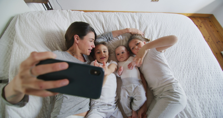Authentic shot of happy mother with her kids are making a selfie or video call to father or relatives in a bed. Concept of technology, new generation,family, connection, parenthood, authenticity | Shutterstock HD Video #1049520961