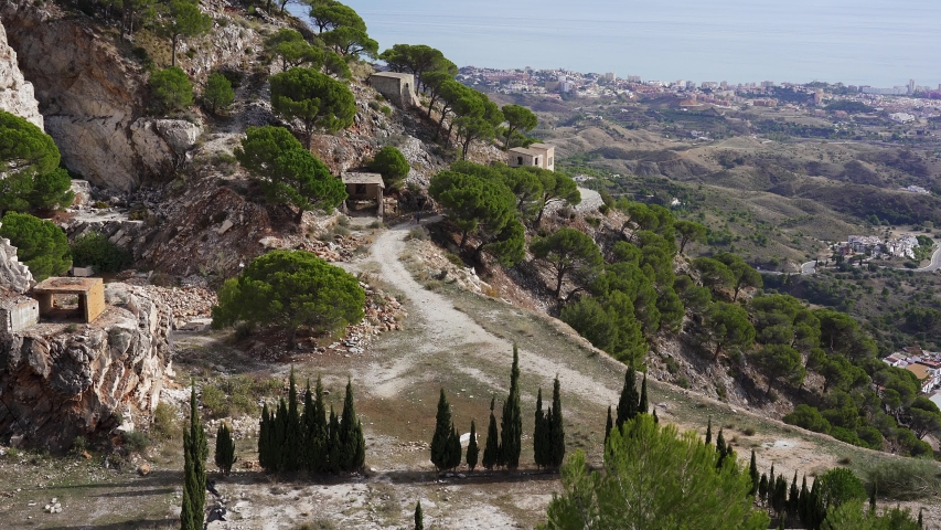 Two distant hikers walk along the excavated hillside of a former Roman quarry in the mountains above the Spanish town of Mijas