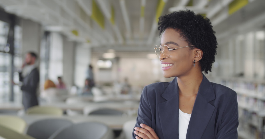 Successful millennial businesswoman in suit smiling and turning head to camera.Young african american female leader office worker standing in modern office. Portraits Royalty-Free Stock Footage #1049523529