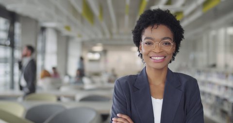 Successful millennial businesswoman in suit smiling and turning head to camera.Young african american female leader office worker standing in modern office. Portraits