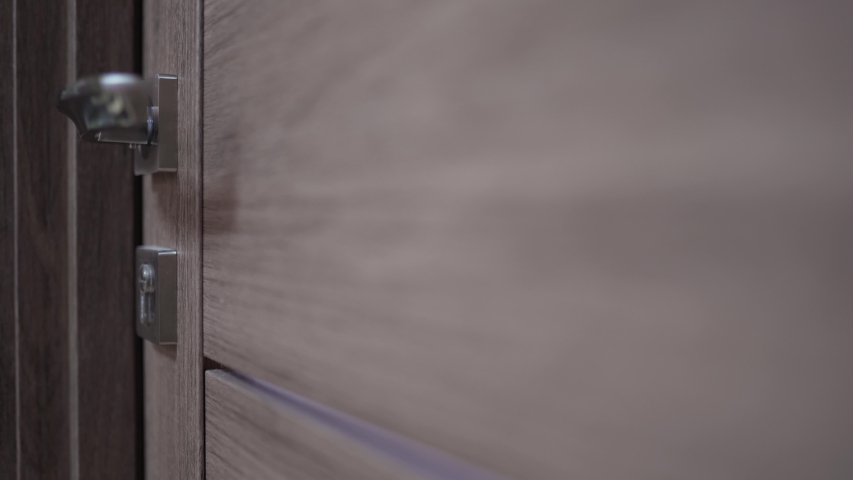 The woman opens the key lock of the door and leaves the room, a close-up static shot. Bright background behind the wooden door Royalty-Free Stock Footage #1049536666