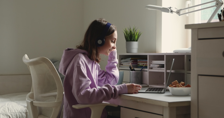 Teenage girl school student wearing wireless headphones conference calling on laptop distance learning at home. Teen schoolgirl chatting by web cam preparing for test or exam with online teacher.