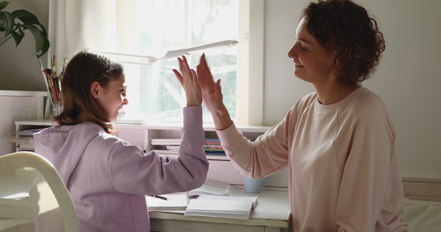 Happy family adult parent mother helping motivating teenage school girl doing homework giving high five. Positive mom and teen daughter studying together having fun sitting at home desk in sunny room. | Shutterstock HD Video #1049543254
