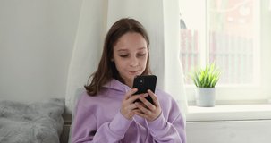 Teenage girl holds smartphone using mobile app at home. Technology addicted teen looking at cell phone chatting in social media, texting messages, watching videos. Teenagers technology overuse concept