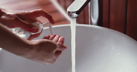 Young woman washing hands with liquid soap sanitizer gel, rinsing with hot water over bathroom sink. Corona virus infection prevention, antibacterial protection hygiene routine concept. Close up view